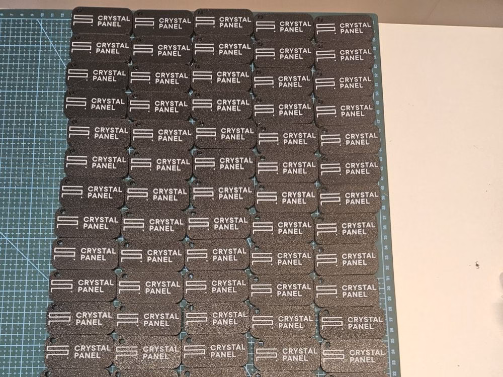 Seria wydrukowanych czarnych breloków z białym logo Crystal Panel ułożonych na macie